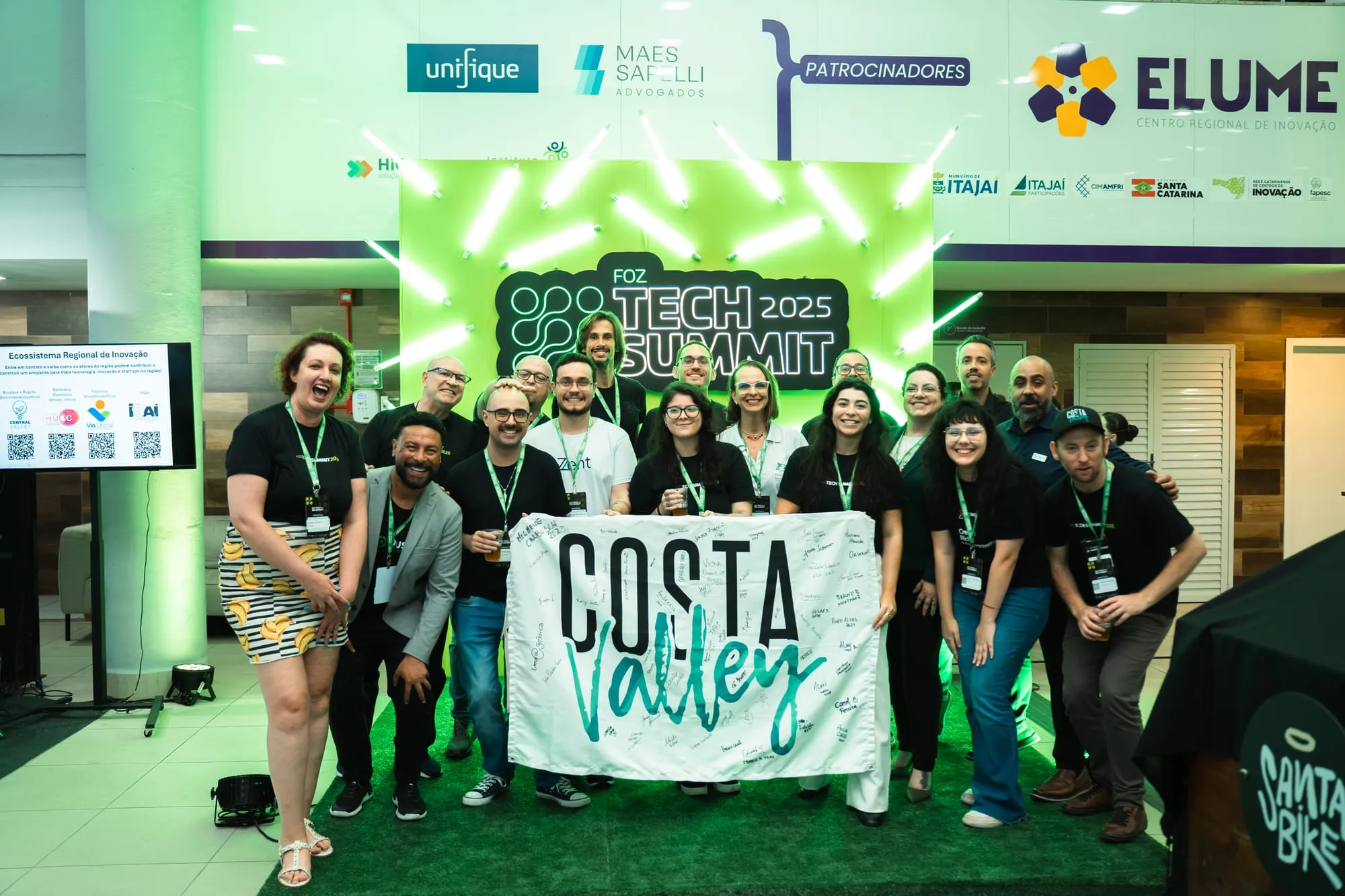 Equipe do evento brinda em frente ao painel iluminado